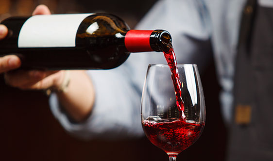 A person pours red wine from a bottle into a clear wine glass.
