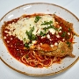 A plate of spaghetti topped with breaded chicken cutlet, marinara sauce, melted cheese, and fresh herbs, served on a speckled white plate.